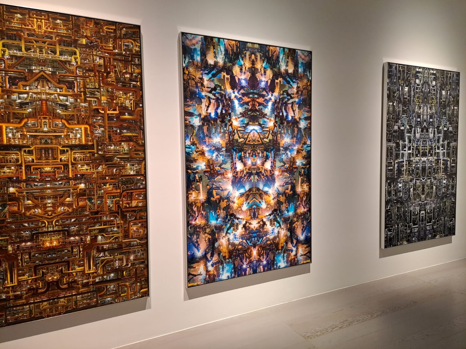 3 quadri su muro bianco, illuminati da dietro. La prima immagine quella a sinistra rappresenta un insieme di tubi generati da un IA per poi essere specchiati e duplicati a mano